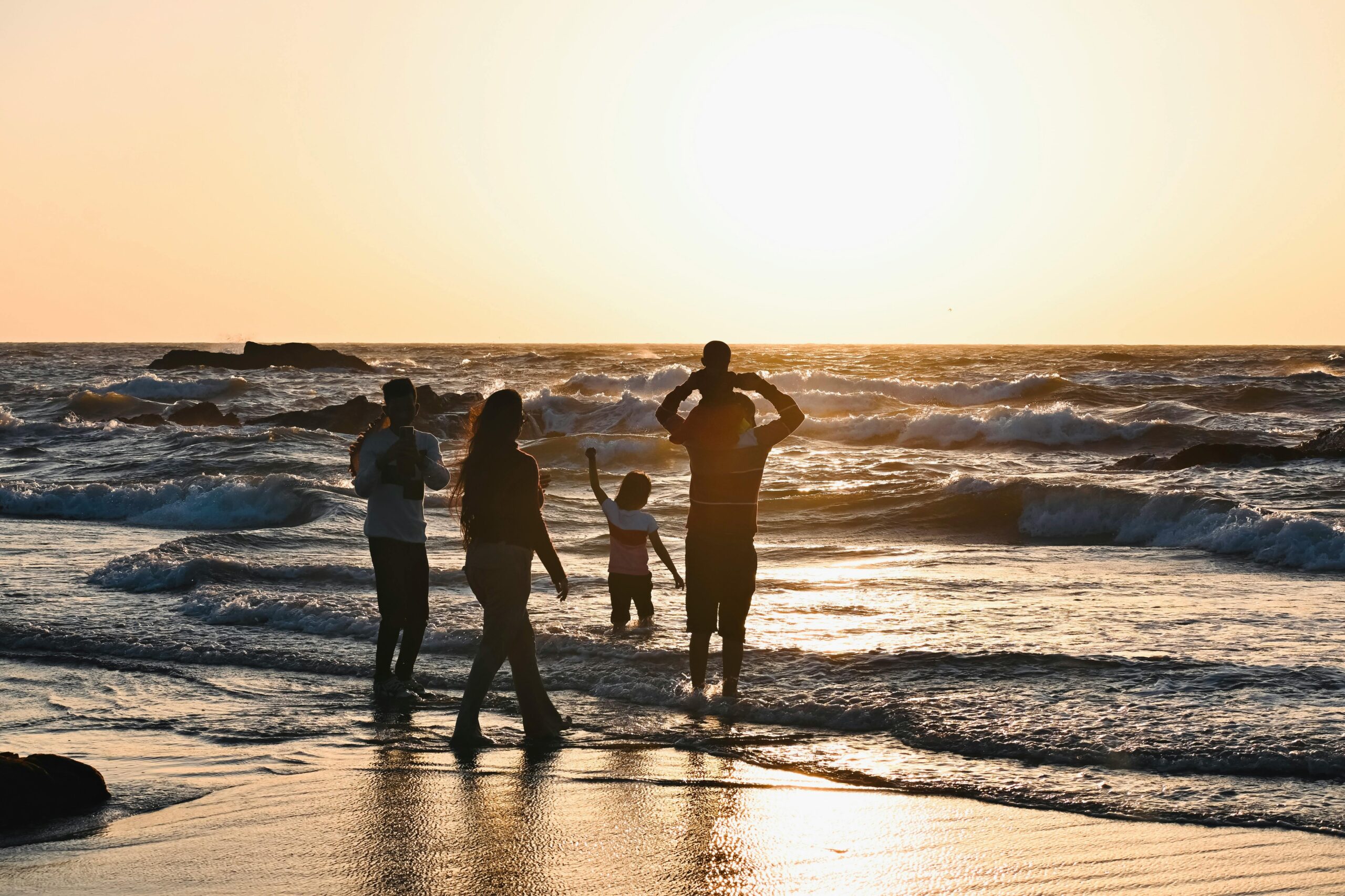 Silhouetted family enjoying a vibrant sunset at a beach in Goa, India.